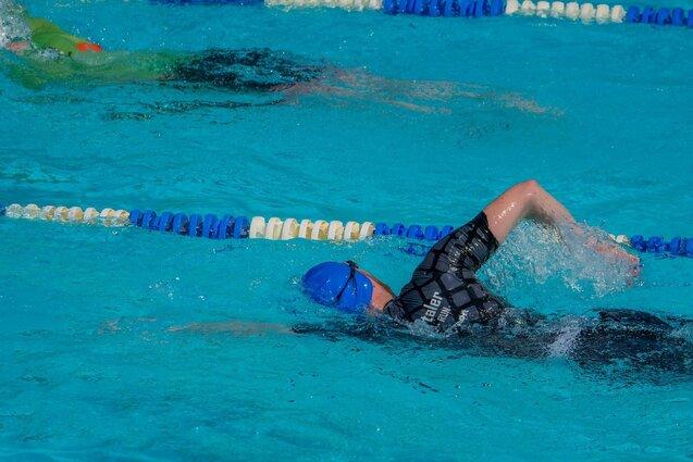 Kraulkurs Schwimmer in blauer Badekappe und schwarzem Anzug beim Kraulen in einem Schwimmbecken mit blauem Wasser.