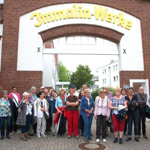 Gruppe von 20 Menschen vor dem Eingang des Immalin-Werks, umgeben von historischen Gebäuden und grüner Landschaft.