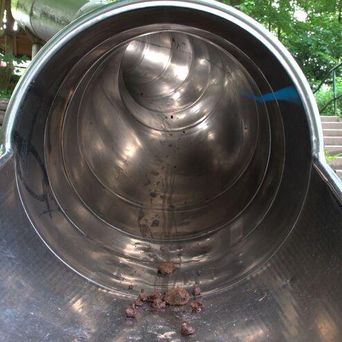 Blick ins Innere einer Edelstahlrutsche, mit Ablagerungen und Treppe im Hintergrund.