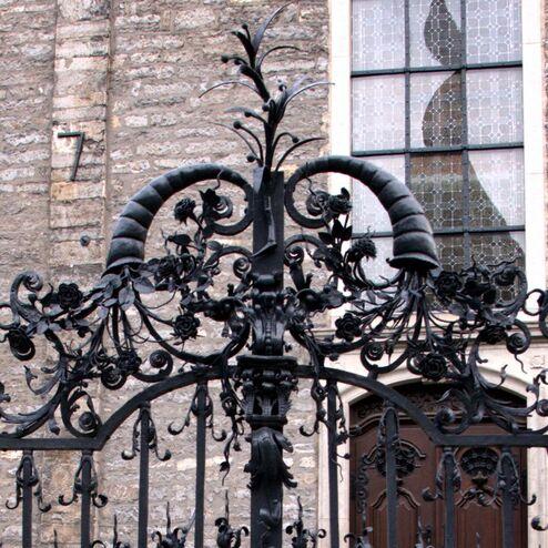 Aufwändig verzierte schmiedeeiserne Tore mit floralem Design und historischem Gebäude im Hintergrund.