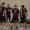 Fünf Volleyballspieler in Schwarz-Rot besprechen sich in einer Sporthalle vor einer grauen Wand.