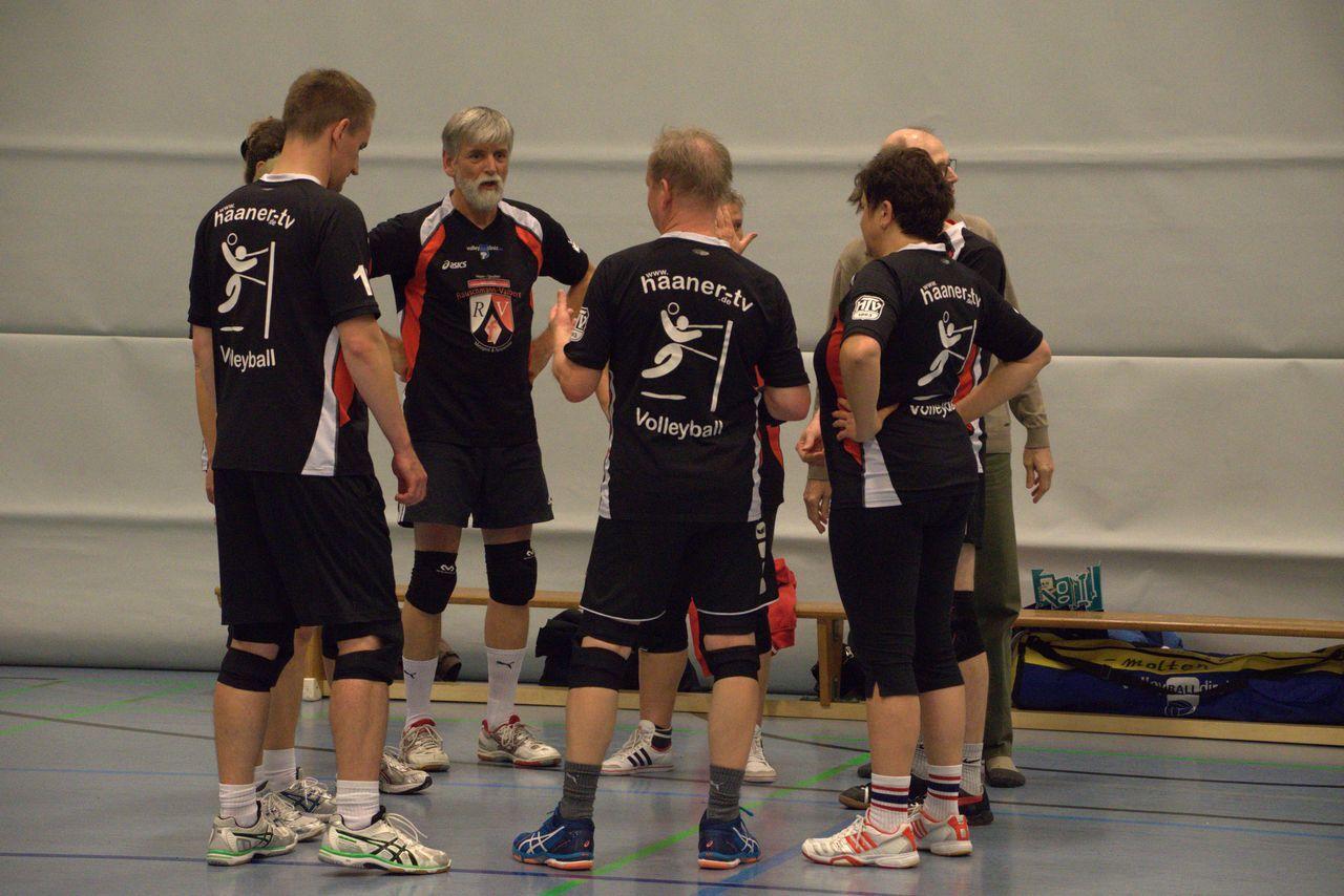 Fünf Volleyballspieler in Schwarz-Rot besprechen sich in einer Sporthalle vor einer grauen Wand.