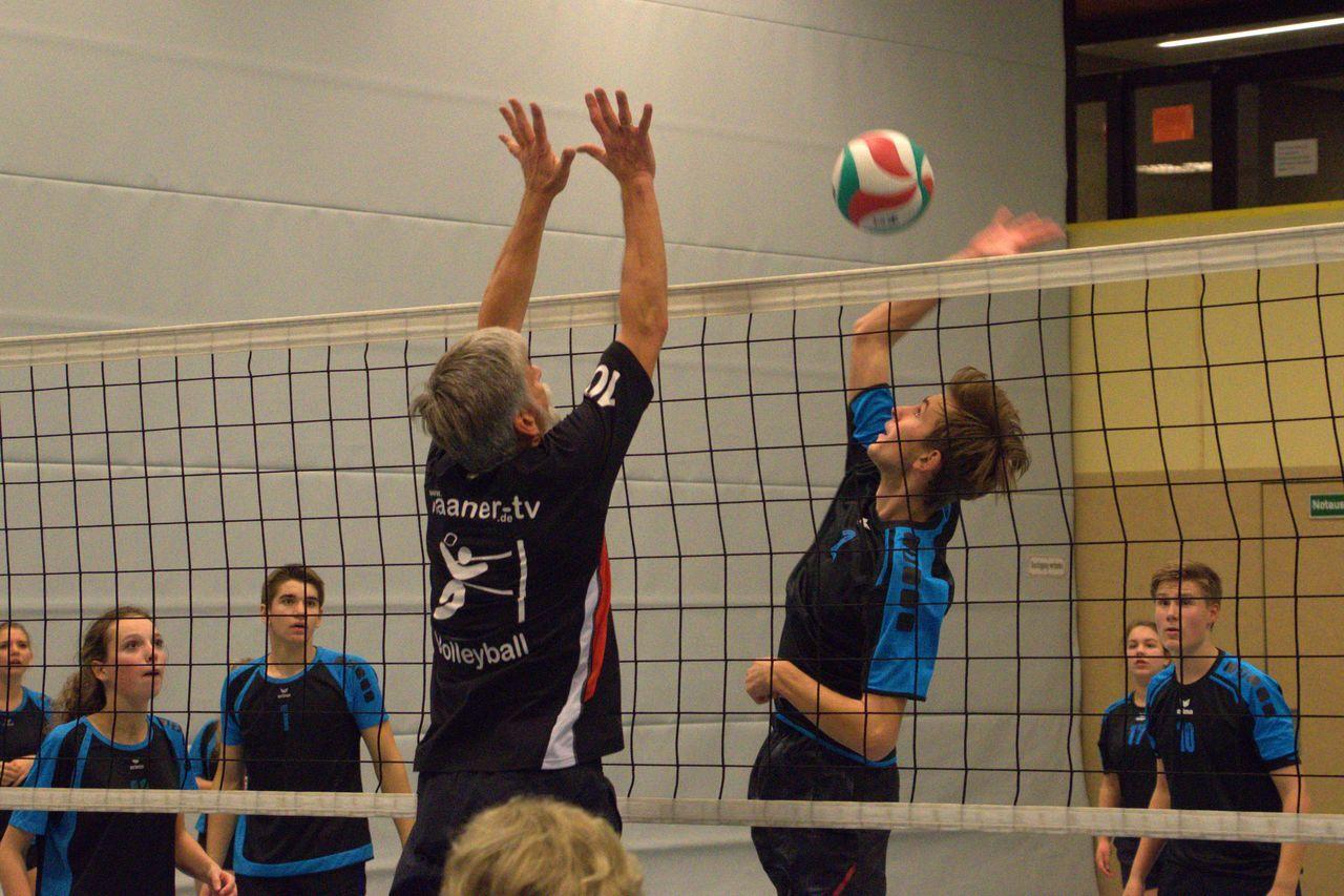 Zwei Volleyballspieler springen an einem Netz, um den Ball während eines Spiels zu treffen. Zuschauer im Hintergrund.
