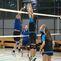 Volleyballspiel in einer Halle, ein Spieler springt zum Blocken, während andere Spieler im Hintergrund agieren.