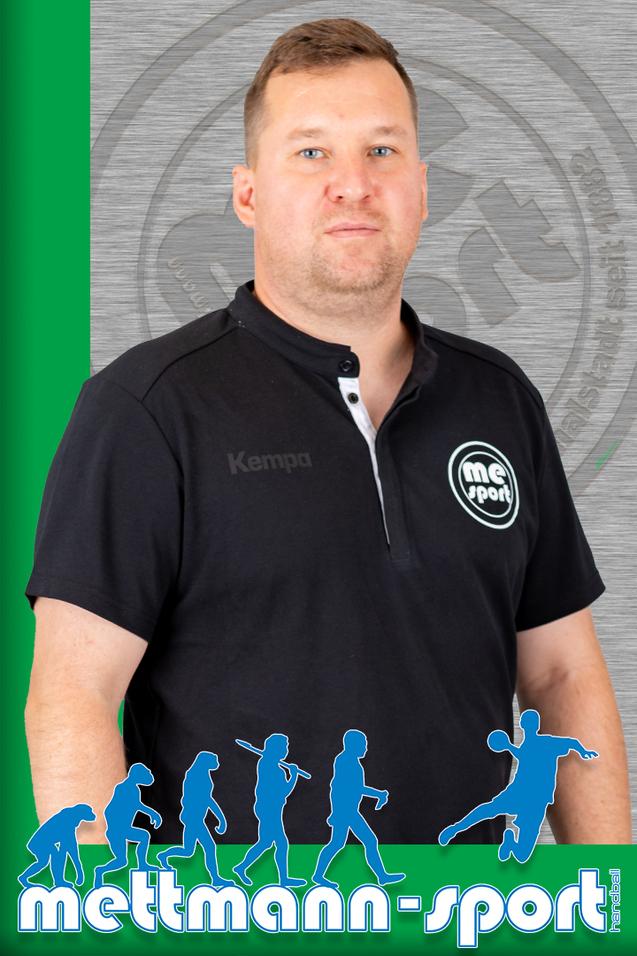 Porträt eines Mannes in einem schwarzen Poloshirt mit Logo, vor einer grauen und grünen Hintergrundgrafik.