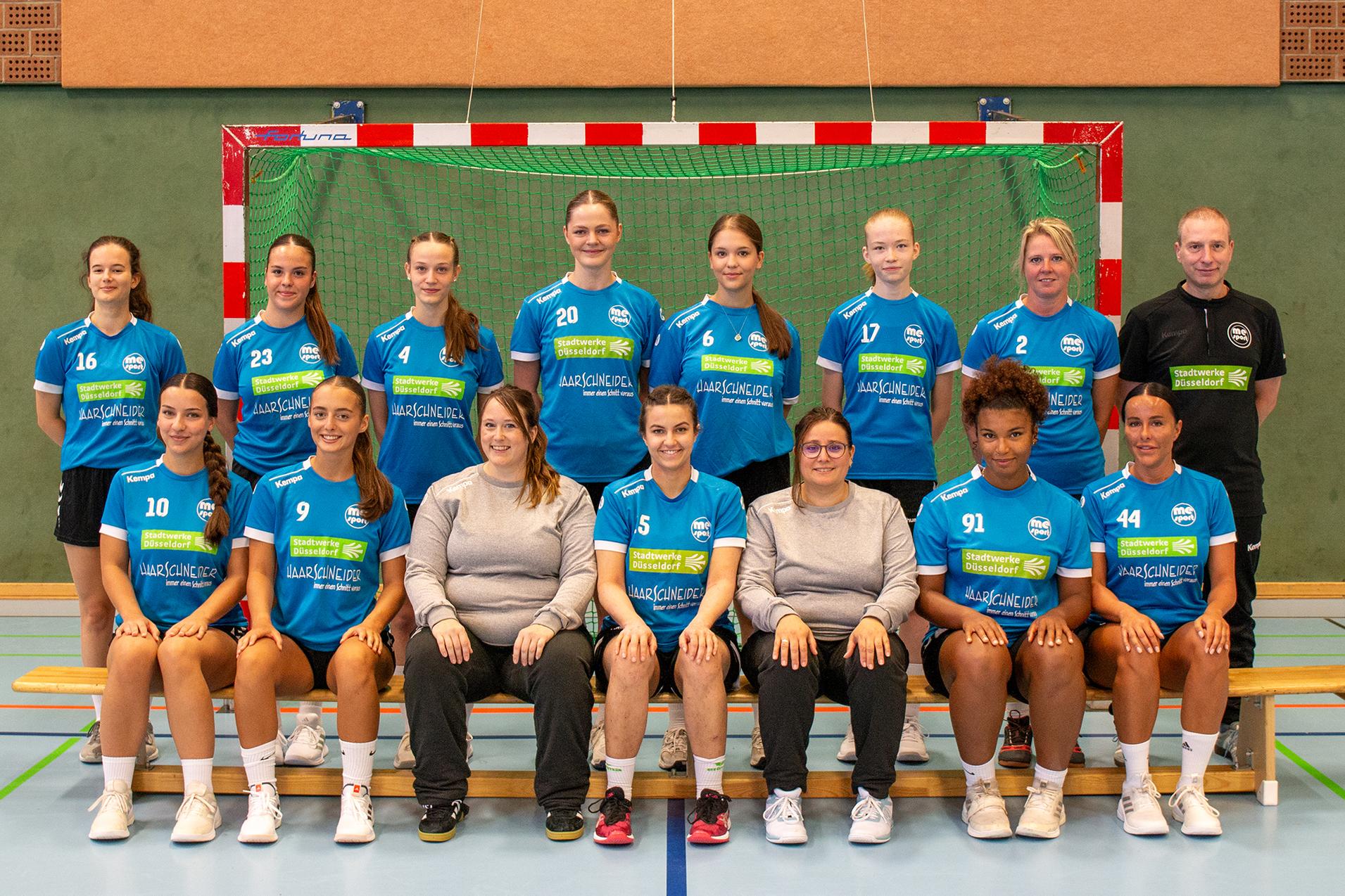 Teambild einer Handballmannschaft in blauen Trikots vor einem Tor auf einem sportlichen Hallenboden.