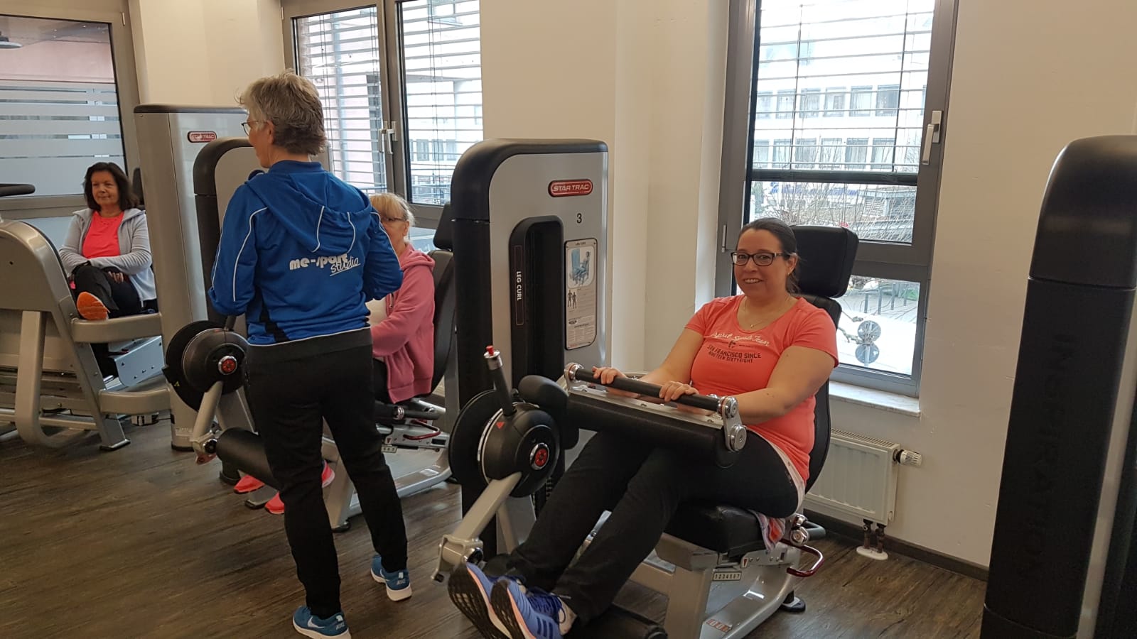 Gruppe von Frauen beim Training im Fitnessstudio, eine Frau verwendet eine Beinpresse, weitere sind im Hintergrund aktiv.