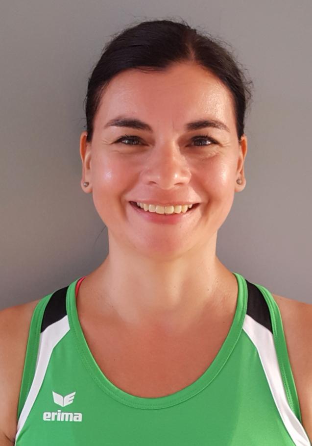 Frau mit kurzem, dunklem Haar trägt ein grünes Sporttop und lächelt vor grauem Hintergrund.