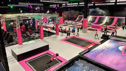 Trampolinhalle mit mehreren Trampolinen, Hindernisparcours und zahlreichen Kindern, die springen und spielen.
