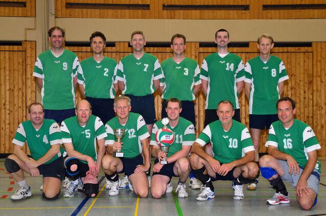Mannschaftsfoto einer Volleyballgruppe in grünen Trikots, mit Pokalen, in einer Sporthalle.