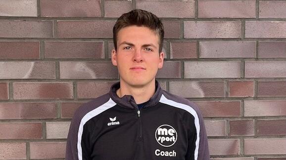 Junger Mann mit kurzem Haar in schwarzem Trainerpullover vor einer gemauerten Wand.