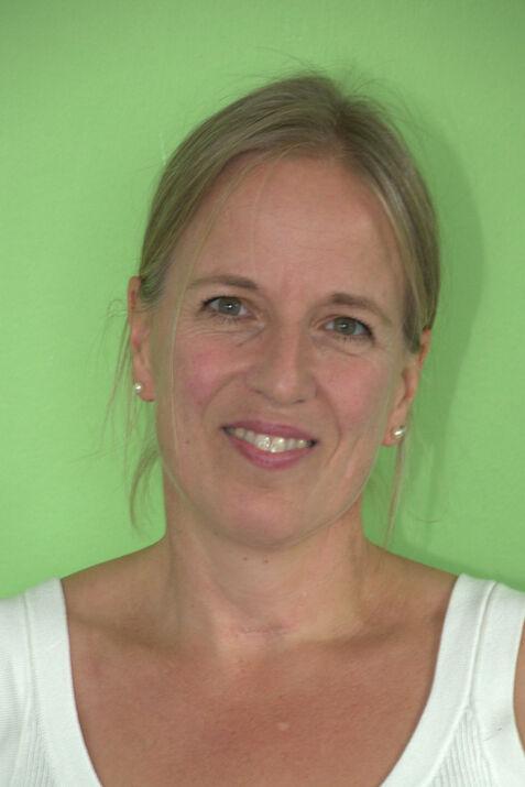 Porträt einer lächelnden Frau mit blonden Haaren vor einem grünen Hintergrund, trägt ein weißes Oberteil.