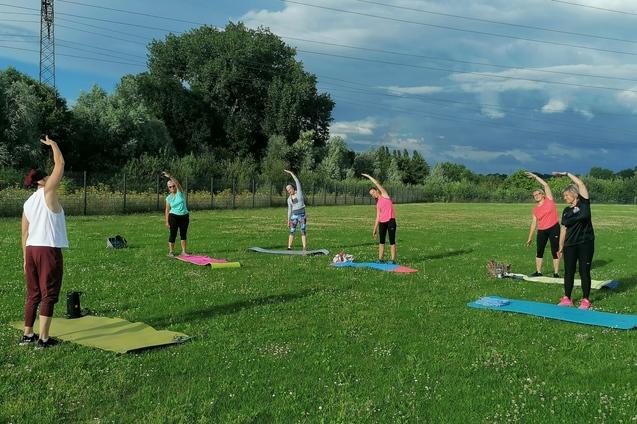 Sport im Park 6 Frauen auf einer Wiese die ihre Matte vor sich liegen haben und Sportübungen machen.