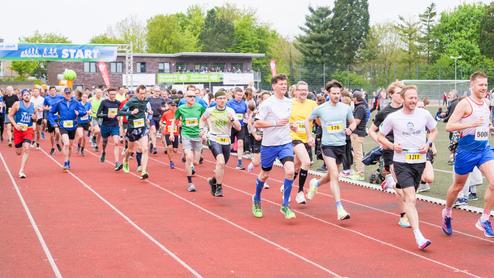 Start eines Laufwettbewerbs mit zahlreichen Teilnehmern auf einer roten Laufbahn unter einem Startbanner.