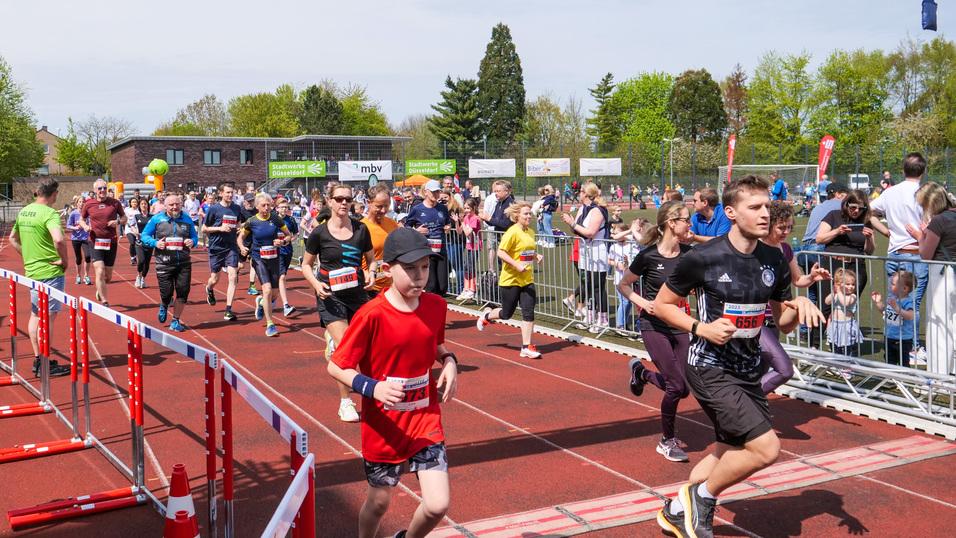 Sportveranstaltung mit Läufern beim Start eines Wettlaufs, umgeben von Zuschauern und einer begrünten Kulisse.