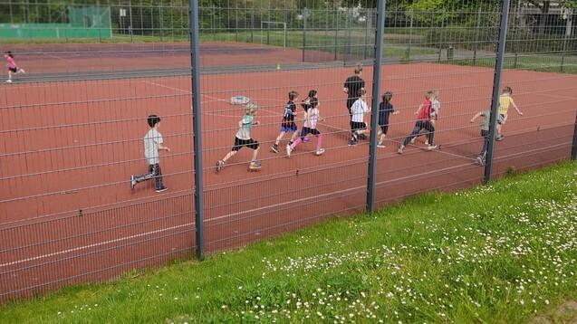 Dutzende Kinder laufen auf einem Weg zwischen Bäumen und Wiesen, während sie ein Sporttraining absolvieren.