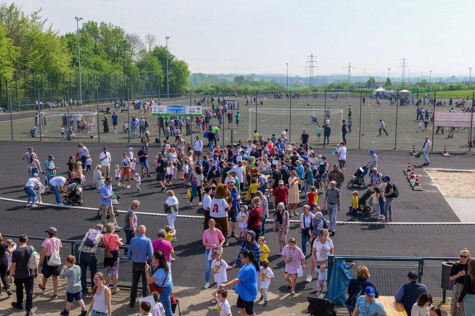 Große Menschenmenge auf einem Sportplatz mit Aktivitäten für Kinder und Familientreffen an einem sonnigen Tag.