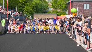 Start Bambinilauf Eine Gruppe von Kindern startet einen Wettlauf, umringt von Zuschauern auf einer asphaltierten Strecke.